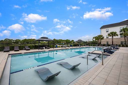 A large outdoor swimming pool with sun loungers and a building in the background.