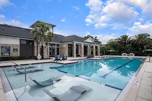 A large outdoor swimming pool with lounge chairs and a building in the background.