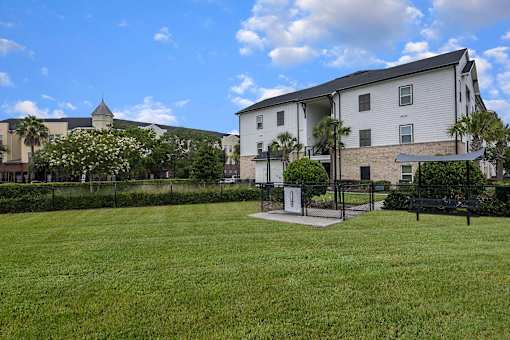 A grassy field in front of a building with a fence and a bench.