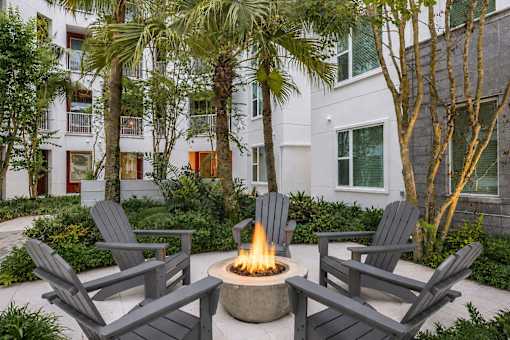 A fire pit sits in the middle of a patio surrounded by chairs and trees.