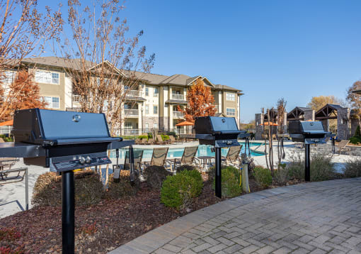 an outdoor pool with barbecue grills and chairs in front of an apartment building