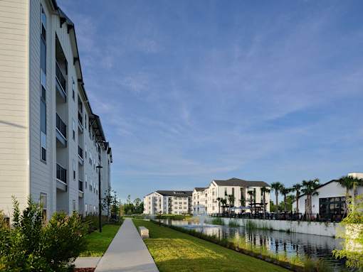 A walkway with grass on either side leads to a building with a waterfront.