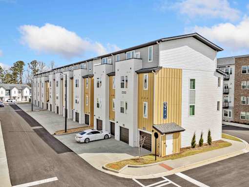 A row of modern townhouses with a white car parked in front of the first one.
