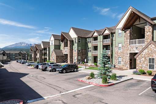 A row of apartment buildings with cars parked in front.