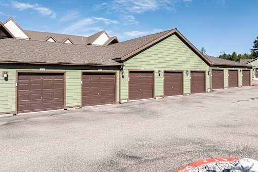 A parking lot with a green building and brown garage doors.
