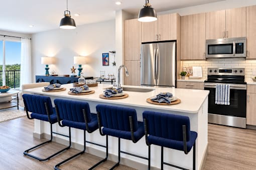 A kitchen with a long white island and blue chairs.