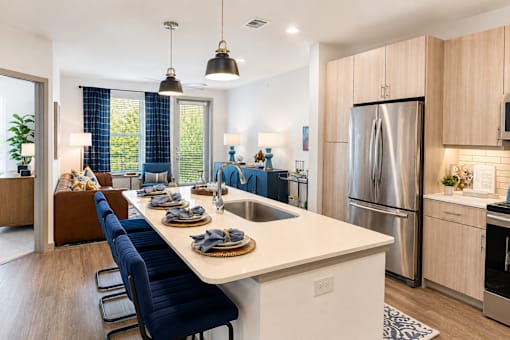 A modern kitchen with a long white island and blue chairs.