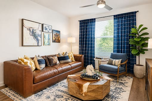 A living room with a brown leather couch, a coffee table with a gift box on it, a blue chair, and a ceiling fan.