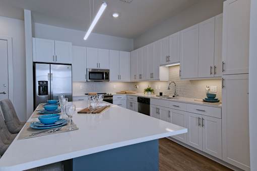 Downtown Memphis, TN, Studios for Rent - The Rise - Gourmet Kitchen with Stainless Steel Appliances, Large Kitchen Island with Seating, Quartz Countertops, White Custom Cabinetry, and Hardwood Style Flooring.