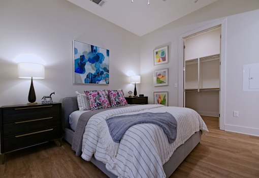 1 Bedroom Apartments in Downtown Memphis, TN - The Rise - Bedroom with White and Gray Bed, Two Nightstands with Drawers and Lamps, Spacious Closet, and Hardwood-Style Flooring.
