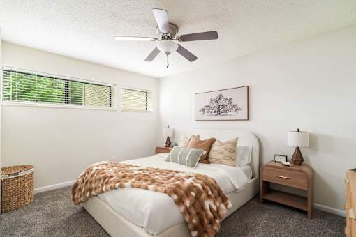 A bedroom with a bed covered in a brown blanket and a ceiling fan above it.