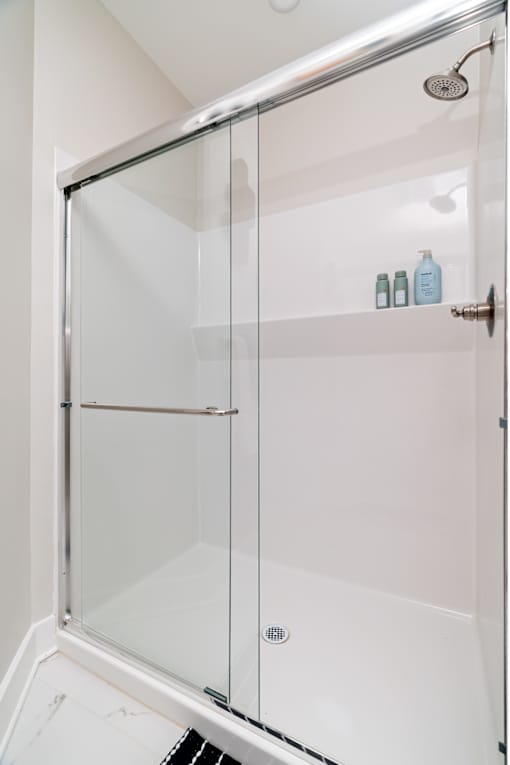 A white shower stall with a glass door and a silver handle.