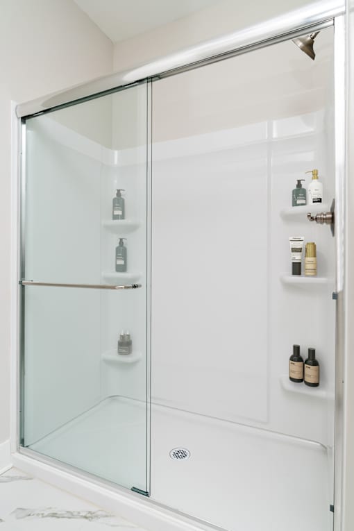A white shower with a glass door and shelves on the wall.