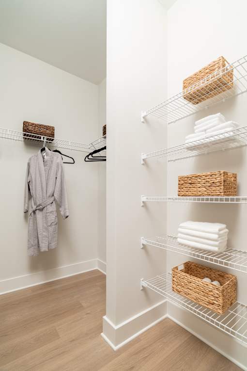 A white bathroom with a towel hanging on the wall and a basket on the shelf.