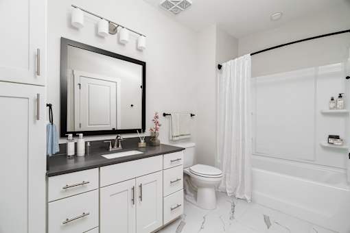 A white bathroom with a sink, mirror, toilet, and bathtub.
