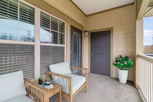 A wooden chair and table are on a porch with a grey door.
