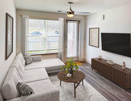 A living room with a grey couch, a wooden coffee table, and a flat screen TV mounted on the wall.