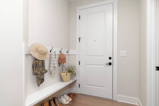 A white door is in a hallway with a bench and shoes on the floor.