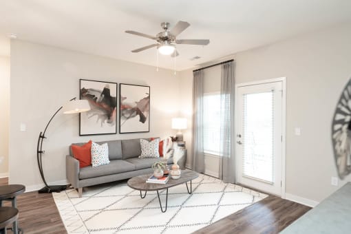 Alcoa, TN, Luxury Apartments with In-Unit Washer and Dryer - Vintage Hunters Crossing - Living Room with Hardwood-Inspired Flooring, Couch, Coffee Table, Floor Lamp, Wall Arts, and Ceiling Fan.