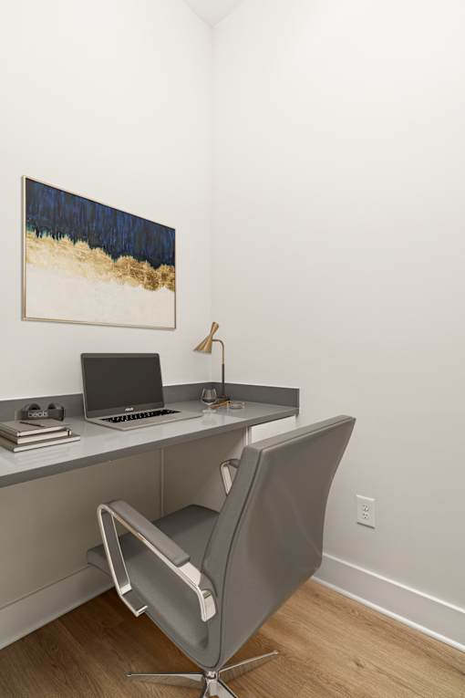 A grey chair is in front of a desk with a laptop on it.