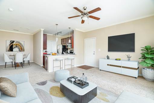 A modern living room with a ceiling fan and a kitchen area in the background.