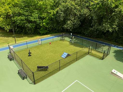 A tennis court surrounded by a fence with a bench and a trash can.