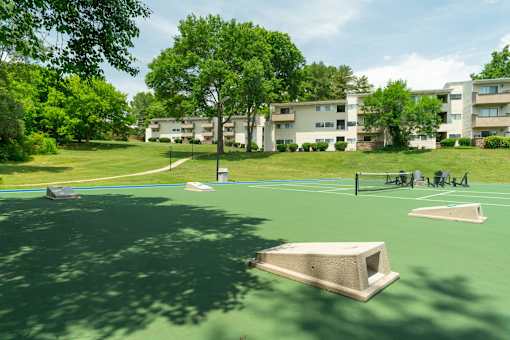 A green tennis court with a bench and a building in the background.