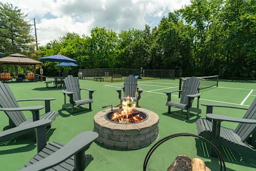 A fire pit sits in the middle of a green lawn surrounded by chairs.