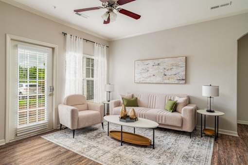 A living room with a beige couch, a chair, a coffee table, and a painting on the wall.