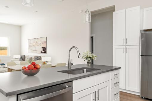 A modern kitchen with a stainless steel sink and a bowl of fruit on the counter.