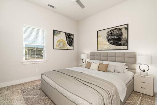A bedroom with a large bed, two lamps, and two framed pictures on the wall.
