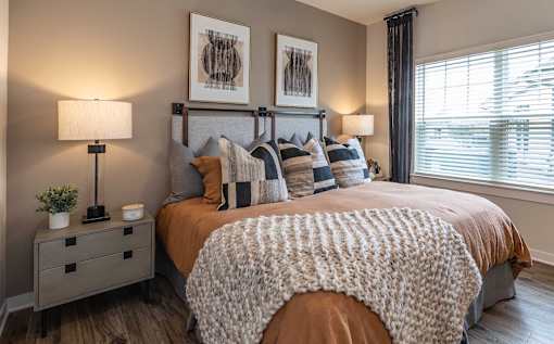 3-Bedroom Apartments in Brunswick, GA - Vintage Brunswick - Bedroom with Hardwood-Inspired Flooring, Large Bed, Nightstands with Lamps, and Large Window