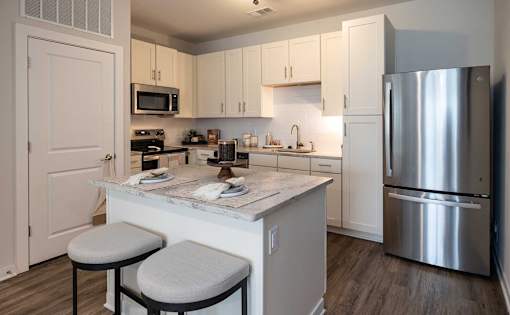 Two-Bedroom Apartments in Brunswick, GA - Vintage Brunswick - Kitchen with Hardwood-Inspired Flooring, Quartz Countertops, Tile Backsplash, Stainless Steel Appliances, White Cabinetry, and Kitchen Island with Stool Seating