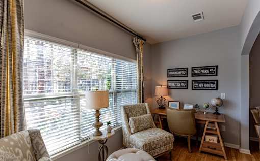 a living room with a large window and a desk with chairs