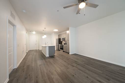 A spacious room with a ceiling fan and a kitchenette in the background.