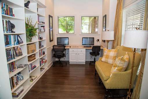 A room with a yellow couch, two laptops, and a bookshelf filled with books.