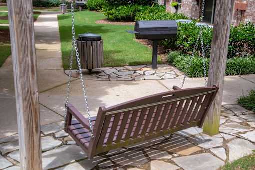 A wooden swing bench is suspended from chains in a backyard.