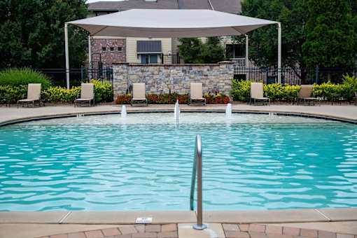 A pool with a white umbrella and a stone wall in the background.