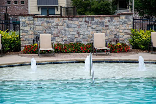 A pool with a stone wall and fountains in the middle.