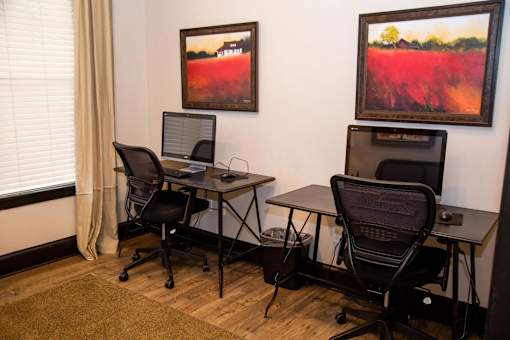 Two computers on desks in a room with two chairs.