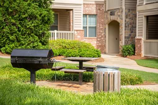 A black mailbox sits on a post next to a picnic table in front of a brick building.
