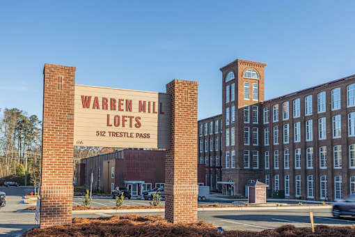 A brick sign that says Warren Mill Lofts in front of a building.
