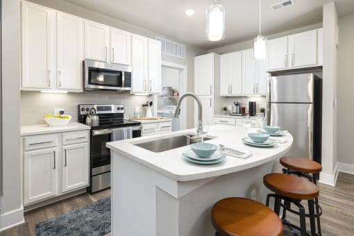 Apartments Near Santa Rosa Beach in Panama City Beach, FL - The Tyde - Kitchen with Hardwood-Style Flooring, Kitchen Island with Seating, Quartz Countertops, Designer Ceramic Tile Backsplash, GE Stainless Steel Appliances, and White 42-Inch Cabinets.
