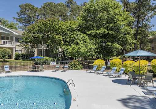 A swimming pool surrounded by trees and chairs.