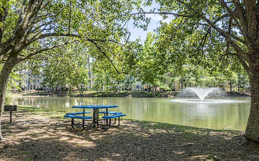 A picnic table is in front of a pond with a fountain.