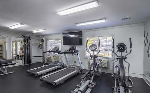 A spacious home gym with treadmills, elliptical machines, and a television.