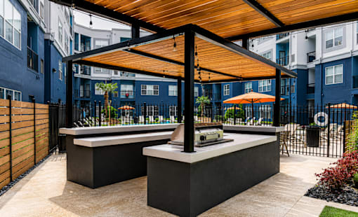A modern outdoor kitchen area with a wooden roof and black countertops.