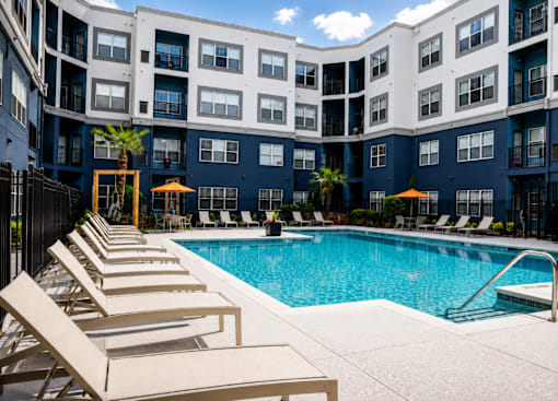 A pool surrounded by lounge chairs and umbrellas in front of a building.