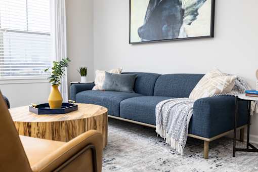 A living room with a blue couch and a yellow vase on a wooden table.