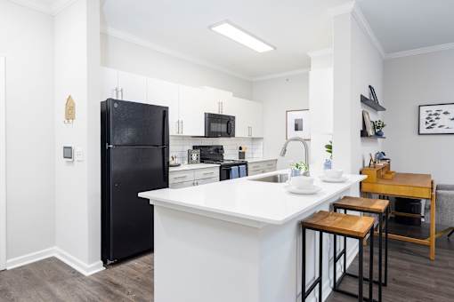 A black refrigerator is in a kitchen with white countertops.